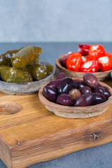 Mediterranean appetizer antipasti tapas bowls with green and calamata olives, feta cheese, stuffed pepper, herbs on wooden plank