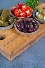 Mediterranean appetizer antipasti tapas bowls with green and calamata olives, feta cheese, stuffed pepper, herbs on wooden plank