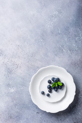 Freshly picked blueberries on white plate on gray stone background. Concept for healthy eating and nutrition with copy space. Top view.