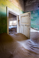 Abandoned room full of sand with a broken open door