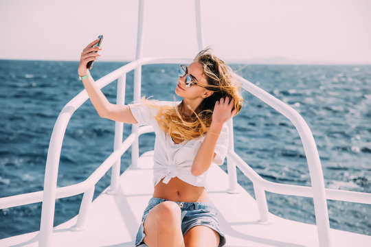 Young beautiful brunette girl making selfie using phone while sitting on the yacht