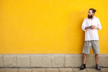 Obraz na płótnie Canvas Tattooed bearded hipster on yellow wall posing outdoor