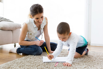 Beautiful young mother and her son drawing at home.