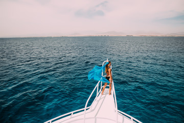 beautiful woman on yacht nose with blue scarf wave on wind. summer time vocation on yacht.