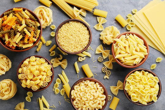 Different kinds of pasta in bowls on grey table