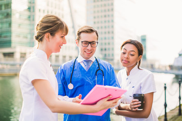 Happy young doctor and nurses look at folder during coffee break, outdoors