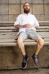 Bearded tattooed hipster lying on a bench. Style and fashion