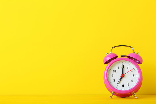 Pink alarm clock on yellow background