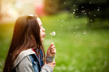 Cute teenage girl in the summer garden blowing a dandelion