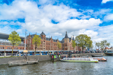 Fototapeta premium The famous Central station with in front lots of tourists getting into canal boats to view the city from the water perspective