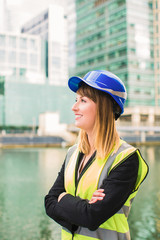 Portrait of beautiful female architect who stands idly, smiles and looks aside, outdoors