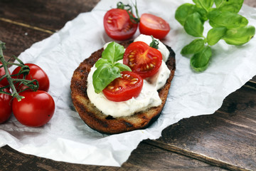 Bread with cream cheese and tomato for lunch table. Sharing antipasti on party or summer picnic time over wooden rustic background.