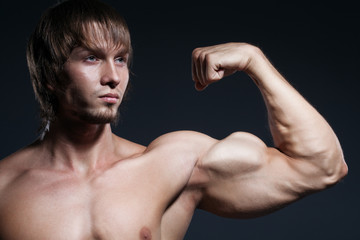 Portrait of strong healthy handsome Athletic Man Fitness Model posing near dark gray wall