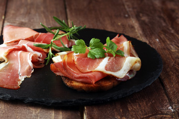 Bread with slices jamon serrano for lunch table. Sharing antipasti on party or summer picnic time over wooden rustic background.