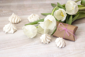 Fototapeta na wymiar Background with white tulips, gift box and meringue cookies on wooden table. Mother's Day background.
