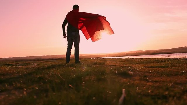 Man plays superhero on sunset sky background. Silhouette of a man in the image of a superman, beautiful sunset. The power concept of the hero looking in the sun.