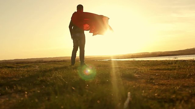 Man plays superhero on sunset sky background. Silhouette of a man in the image of a superman, beautiful sunset. The power concept of the hero looking in the sun.