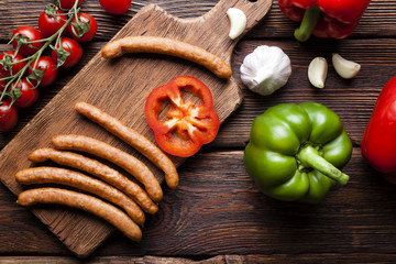 Raw sausage and vegetables on wooden board