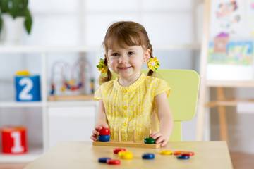 Kid girl playing with logical toy on desk in nursery room or kindergarten. Child arranging and...
