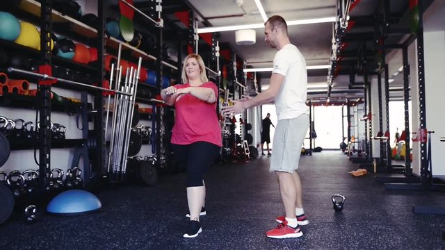 Overweight woman with personal trainer in modern gym.