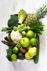 Boxed green fruits and vegetables, apples, pears, broccoli, peas, cauliflower, beans, asparagus, kiwi, avocado, pineapple on white table, top view, selective focus. One colour, healthy eating concept