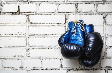 Fototapeta Pair of old blue and black boxing gloves hanging on white brick wall. obraz