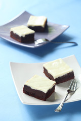 Brownie Goat Cheesecake Squares on two plates, on blue background.