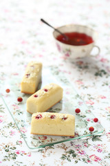 White Chocolate Financiers with Wild Strawberries on transparent glass board and cup of fruit tea, on white floral background.