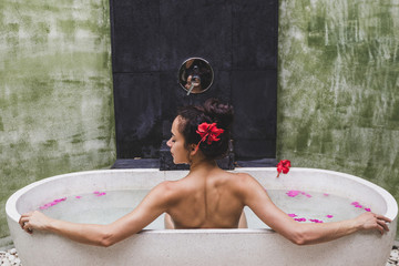 Woman relaxing in round outdoor bath with tropical flowers, organic skin care, luxury spa hotel,...