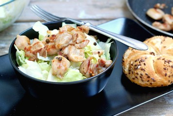 Fresh salad from lettuce and pieces of fried chicken in black bowl