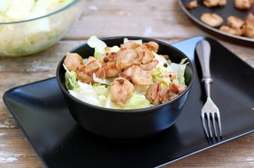 Fresh salad from lettuce and pieces of fried chicken in black bowl