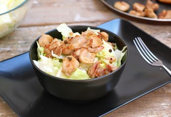 Fresh salad from lettuce and pieces of fried chicken in black bowl