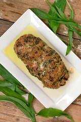 Meat loaf with fresh green buckrams leaves on white plate on wooden background