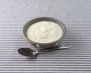 Bowl of vanilla yogurt with a spoon in front atop a blue striped tablecloth.