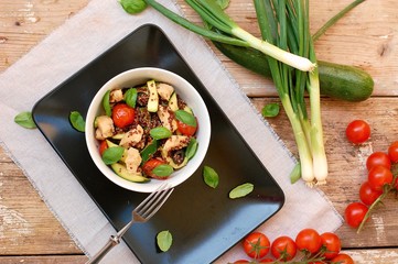 Gluten free food with red quinoa, chicken fillet, tomato,zucchini, olive ,basil leaves and spring onion in white bowl on wooden background