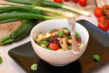 Gluten free food with red quinoa, chicken fillet, tomato,zucchini, olive ,basil leaves and spring onion in white bowl on wooden background