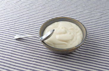 Bowl of vanilla yogurt with a spoon on a blue striped tablecloth.