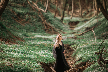 Pretty blonde woman walks in black coat on the green grass