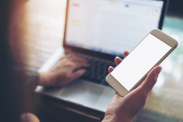 Mockup image of business woman holding mobile phone with blank white screen with latop on wooden table in cafe