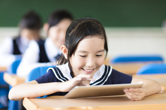 smiling little girl using tablet pc in classroom