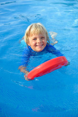 Fototapeta na wymiar Smiling little boy has fun with floating board in swimming pool