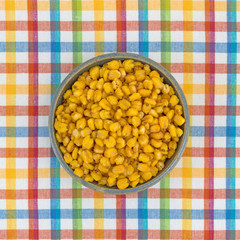 Toasted corn nuts in an old stoneware bowl on a colorful cloth place mat.