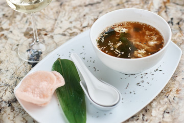 Crab soup served in white ceramic bowl with spoon, green leaf. pink crab chips and glass of white wine.