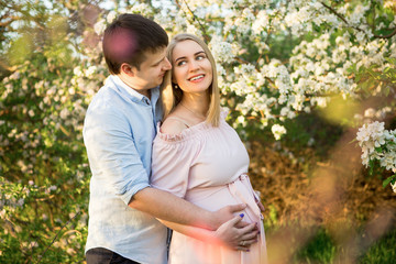 Young parents in a spring park at sunset. Pregnant woman.