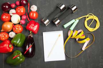 Sport and diet. Healthy lifestyle. Vegetables, dumbbells  notebook. Peppers, tomatoes, garlic, onion  radish on a black background