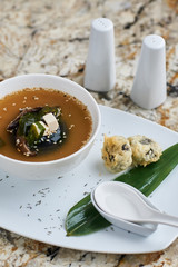 Japanese cuisine. Delicious miso soup with shiitake mushrooms served in white ceramic bowl with spoon, green leaf, salt shaker and pepper-castor