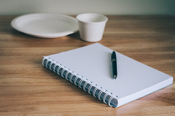 Blank notebook and pen on wooden table with disposable dish and cup,  writing concept, select focus and vintage color effect
