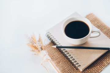 Coffee and note book on white table.