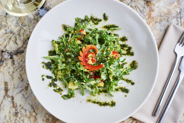 Salad with couscous, cherry tomatoes, avocado and mozzarella served on white plate. Salt shaker, pepper-castor and knife and fork on napkin on marble table