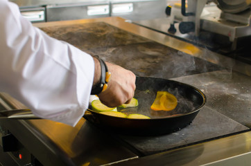 The chef of the restaurant prepares fried vegetables in the pan in the kitchen.